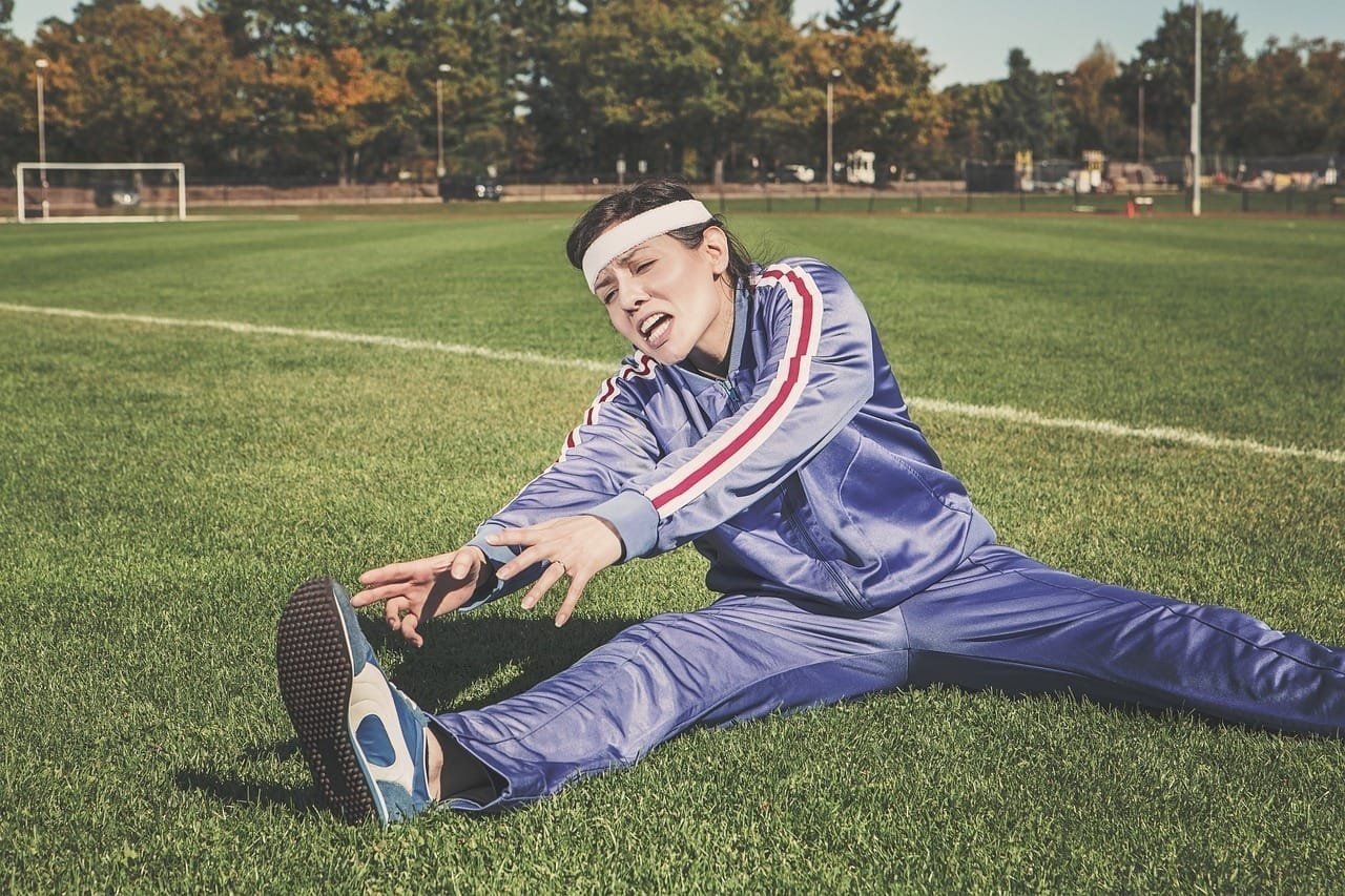 Frau in Sportkleidung dehnt sich auf einem Sportplatz