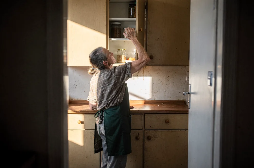 Mann um die 50 trainiert zu Hause mit einem leichten Widerstandsband am Türrahmen, Ellenbogen eng am Körper