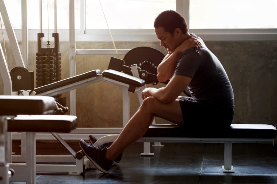 Training bei Rückenschmerzen - dunkelhäutiger Mann auf einer Hantelbank im Fitnessstudio hat Rückenschmerzen Nackenschmerzen