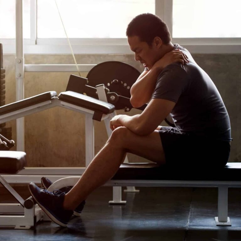 Training bei Rückenschmerzen - dunkelhäutiger Mann auf einer Hantelbank im Fitnessstudio hat Rückenschmerzen Nackenschmerzen