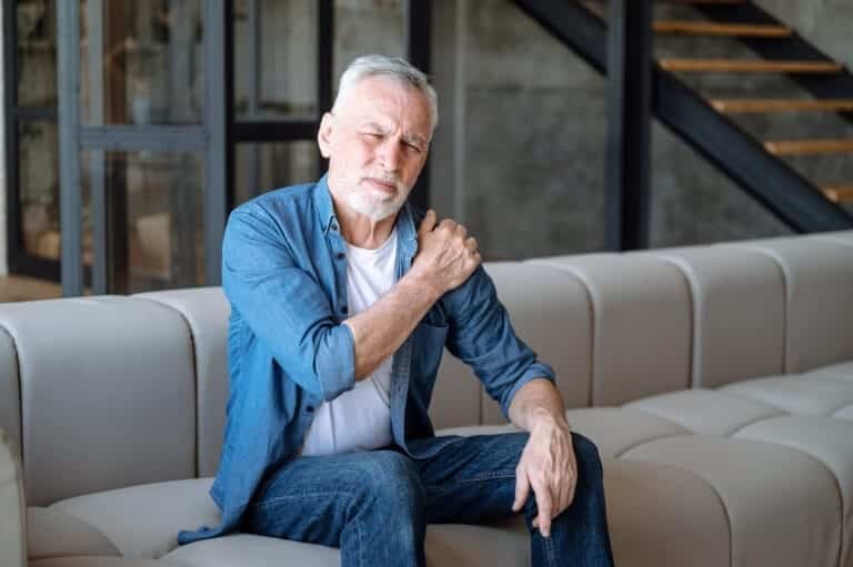 Was sind eigentlich Schmerzen und wie wirst du wirklich schmerzfrei? 1 Mann mit Rückenschmerzen und Gelenkschmerzen sitzt auf einer Coach