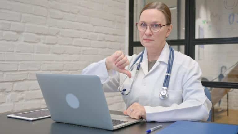Diagnose vom Arzt bei Rückenschmerzen - Thumbs Down by Old Lady Doctor Using Laptop