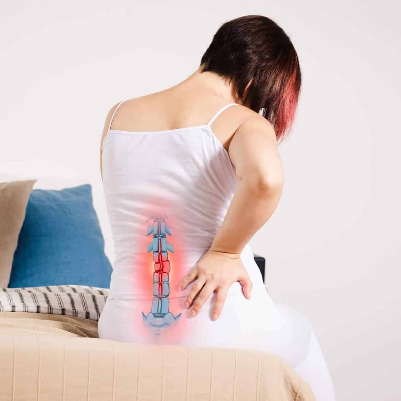 Junge Frau sitzt auf dem Bett und hält sich den schmerzenden unteren Rücken