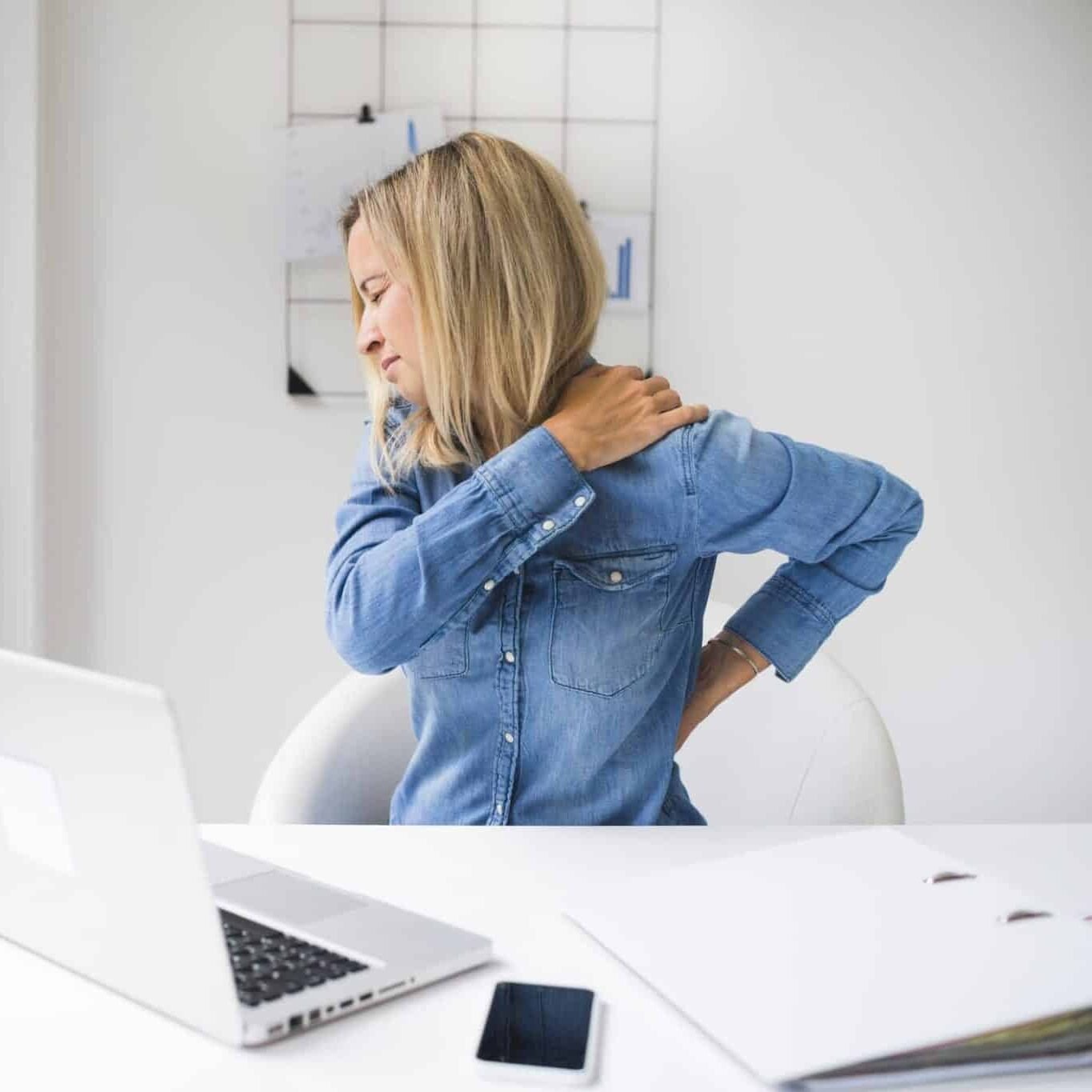 Junge Frau im Büro hat Rückenschmerzen und hält sich die Lendenwirbelsäule